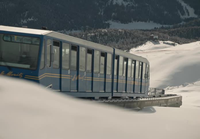 Blue and white funicular train glides smoothly along the tracks through stunning snowcovered alpine scenery