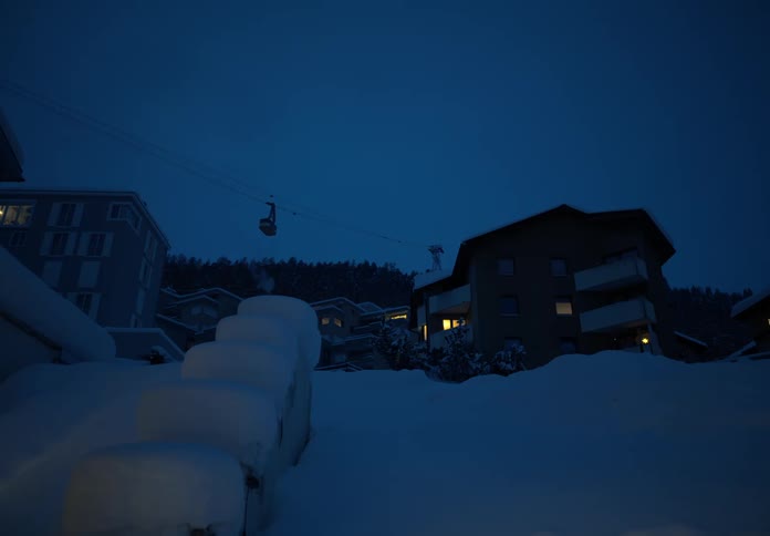 A cable car glides across a twilight sky above a snowcovered village lit by warm window glows