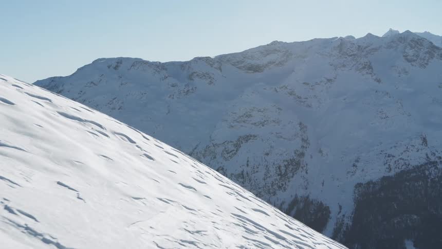 Aerial landscape of a snowy mountain valley against a clear blue sky