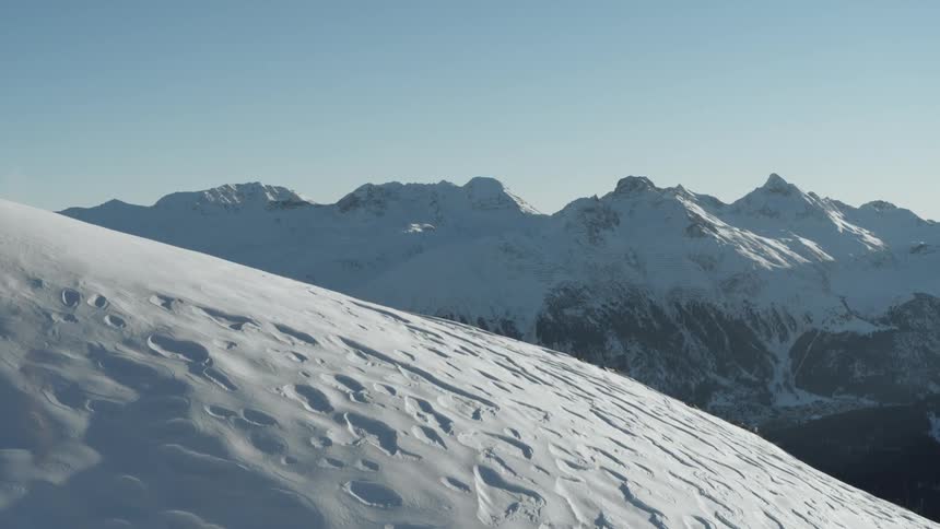 Aerial view a snowcapped mountain range with a charming village nestled in the valley below under a clear blue sky