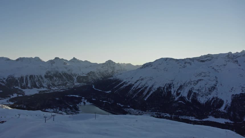 Aerial view of snow capped mountains bathed in the warm light of sunset at a ski resort with a valley and lake nestled amidst the peaks