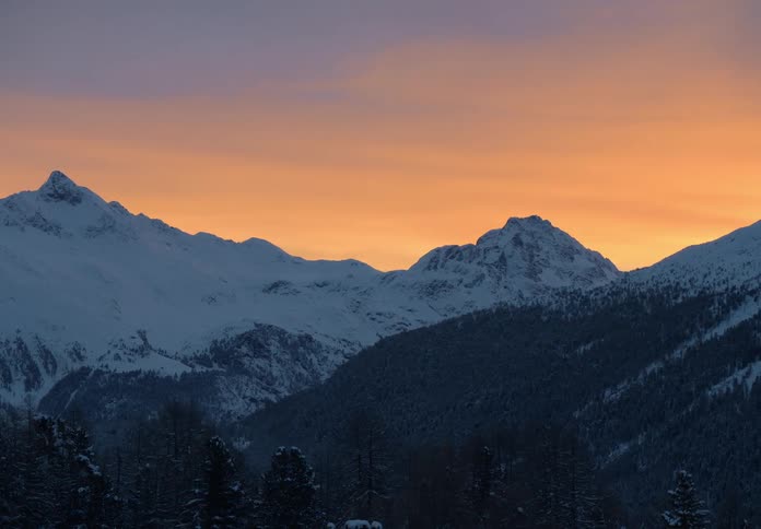Snowcapped mountains at dusk lit by a vibrant orange and gold sky