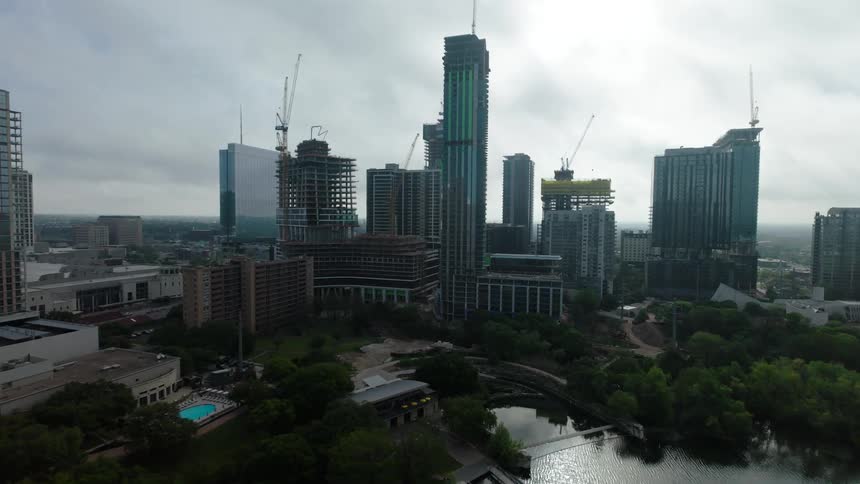 Construction cranes build a skyscraper in a waterside city on an overcast day