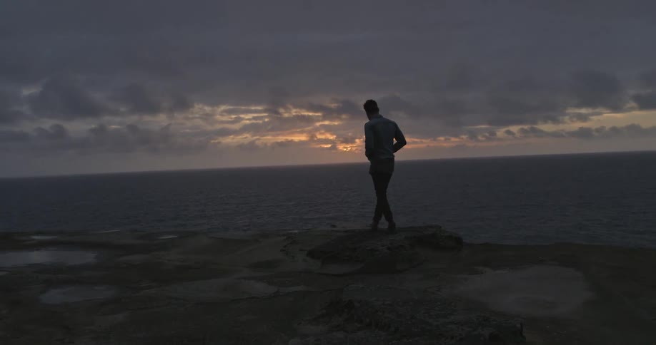 A man walking near the ocean at dusk