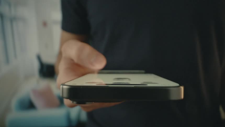 A man is standing in a room scrolling on his phone