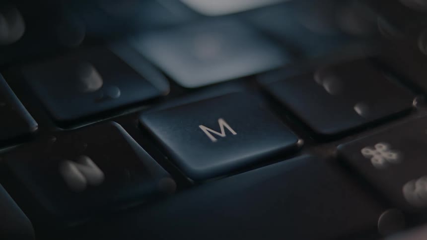 A close up shot of a keyboard with a focus on the m key shows a finger pressing the key repeatedly