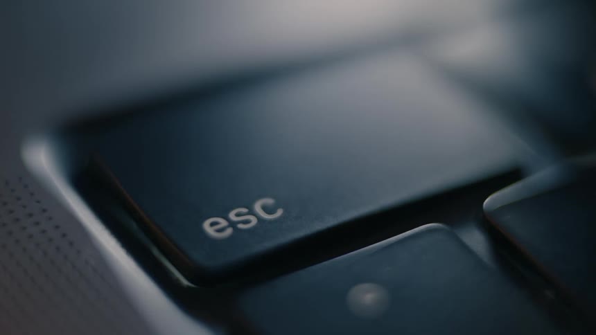A finger pressing the esc key on a keyboard