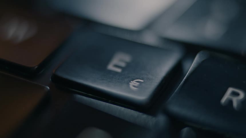 A blurred close up focuses on the e key with the euro symbol on a keyboard which is then pressed three times by a finger