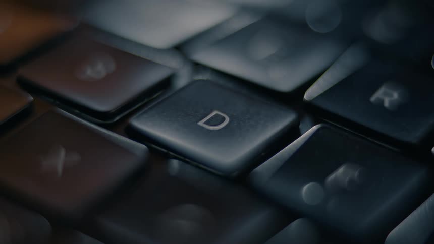 A macro shot with a shallow depth of field shows a finger pressing the d key on a keyboard surrounded by other blurred keys and bokeh highlights