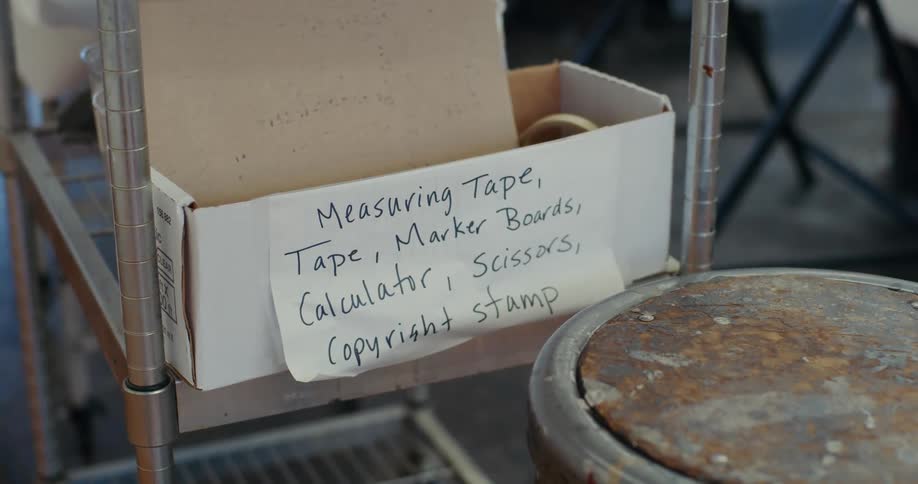 A box with a list of supplies sits on a shelf as a person walks in the background