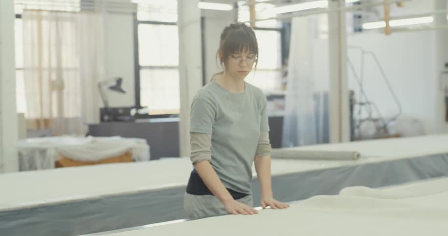 Woman in a light gray top standing in a spacious well lit workspace arranging a large sheet of material on a table