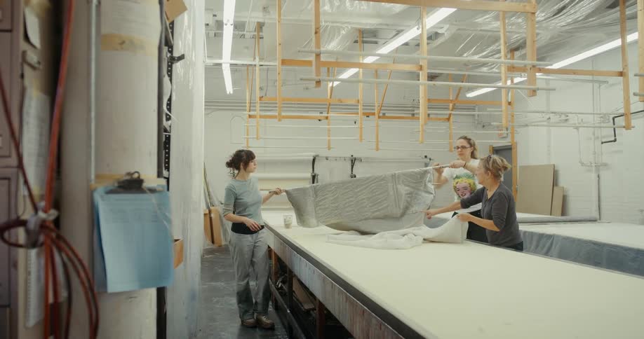 Women move fabric down a long table in a workshop
