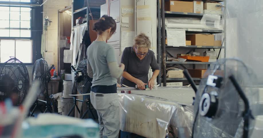 Two women talking and working on a plastic surface in a warehouse