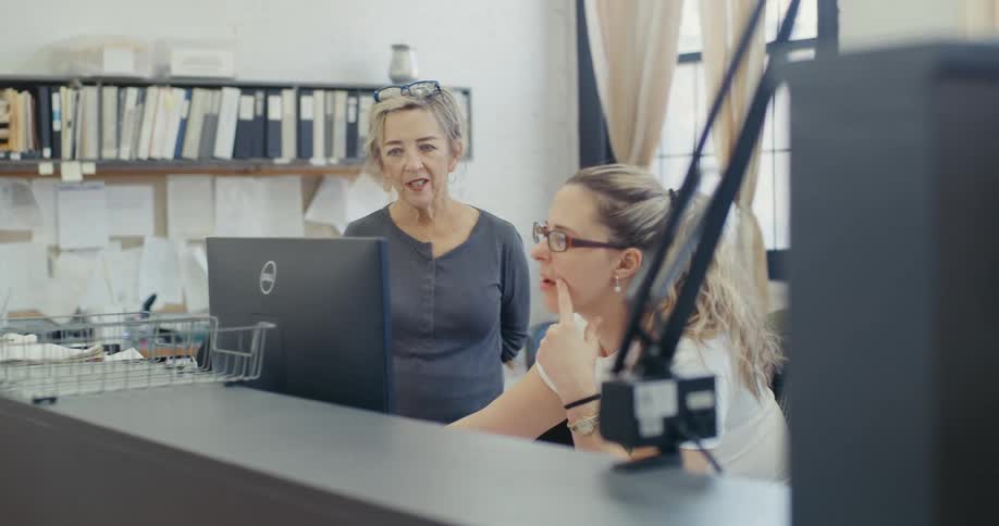 Two women in a workspace talking in front of a computer screen