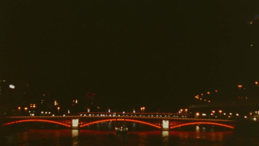 Red lights highlight a bridge that crosses a river in an urban area at night