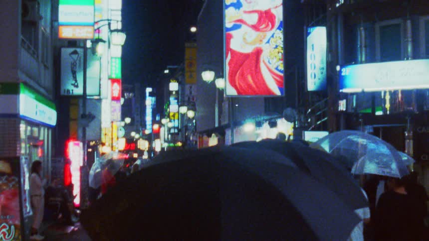 A busy illuminated street at night with people holding umbrellas under vibrant neon signs
