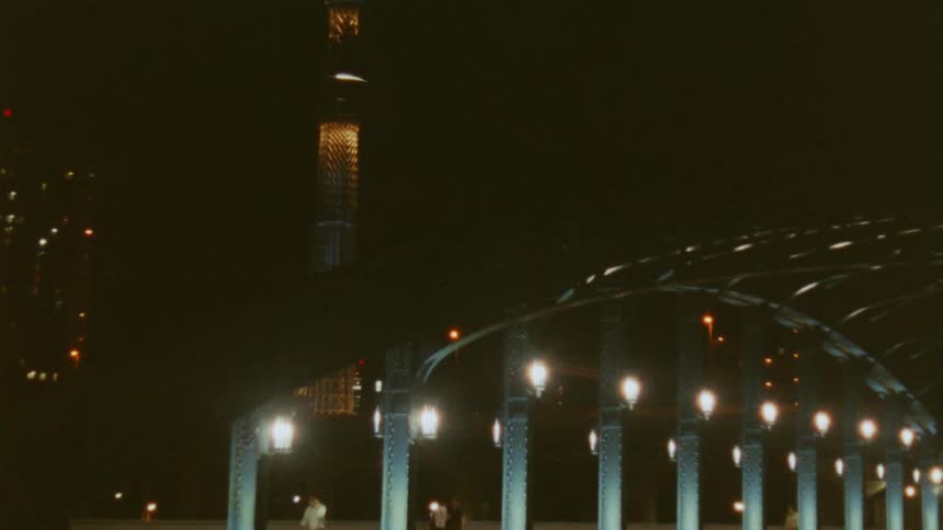 Pedestrians and vehicles cross a bridge near a tower in the city at night