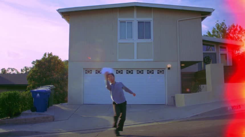 Man dancing next to a house while balancing a paper in his hands