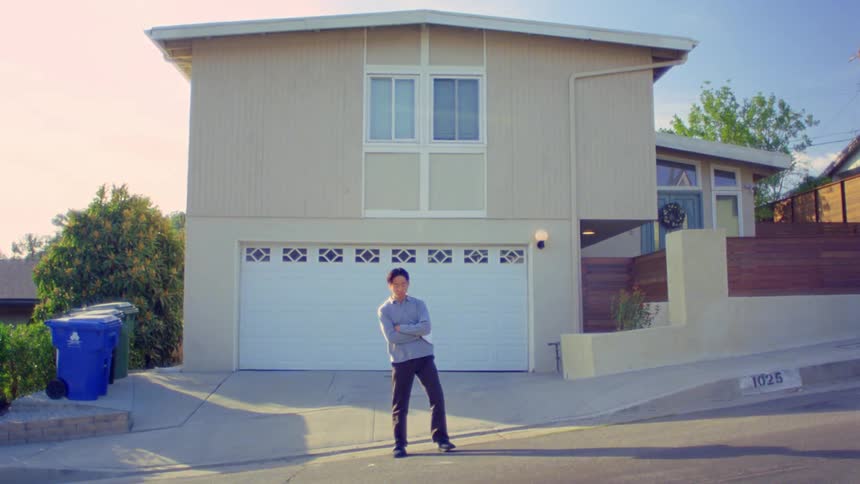 A man stretches as he stands in the street in front of a house