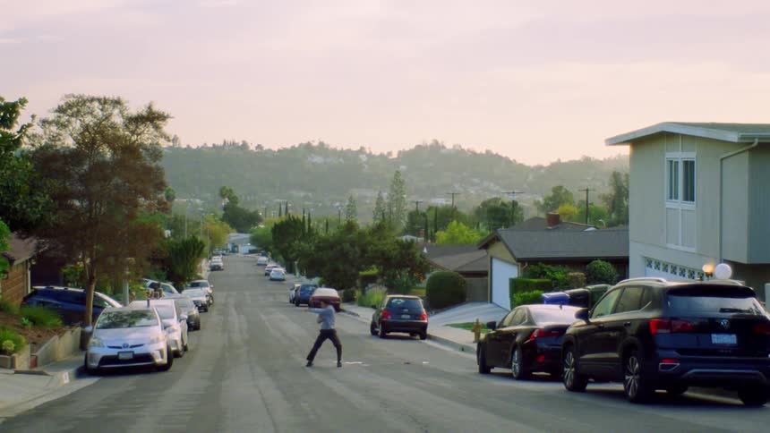 Man dancing in the middle of a street surrounded by parked cars