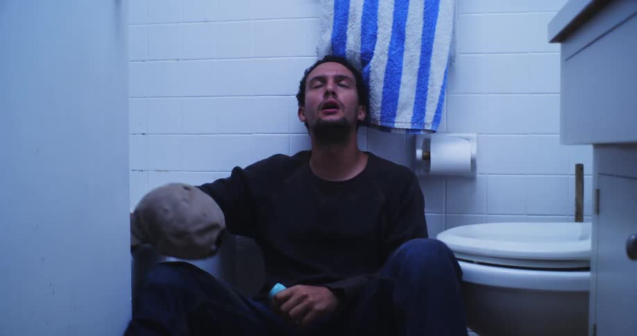 Man rummaging through a bathroom cabinet and sitting depressed