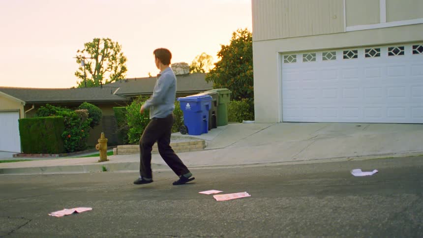 A young asian man dances in the street in a residential neighborhood with papers strewn around him