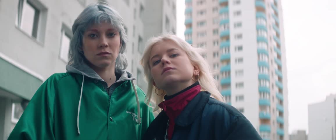 Two teenage girls looking at each other one with blonde hair and the other with light blue hair