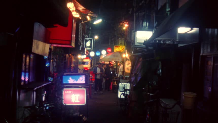 A vibrant illuminated street in an urban area at night with neon signs in japanese and people walking