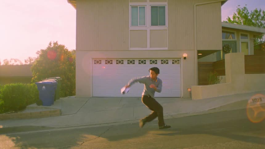 A person is dancing on a sloped street in front of a house with a white garage door