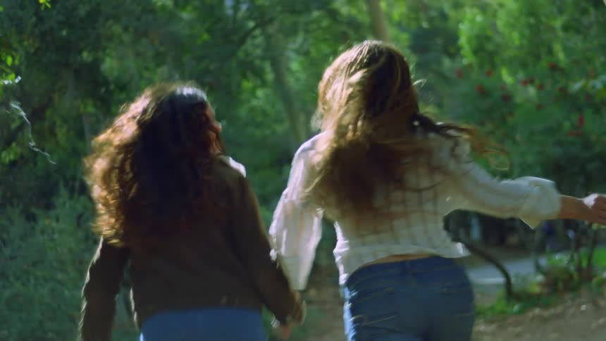 Two women hold hands while running toward the trees