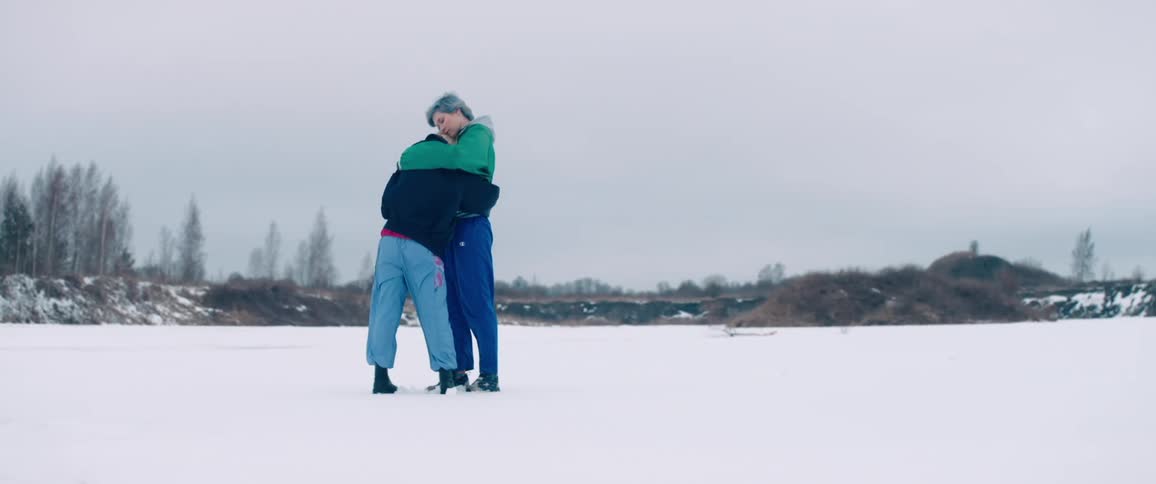 Two women hug as they stand in an open snowy field