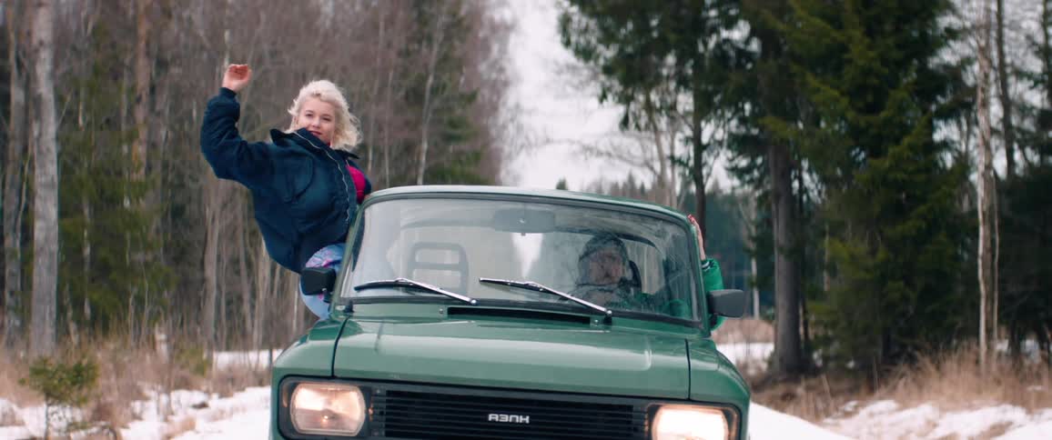 A woman hangs out of the car window as the driver waves her arm out the window