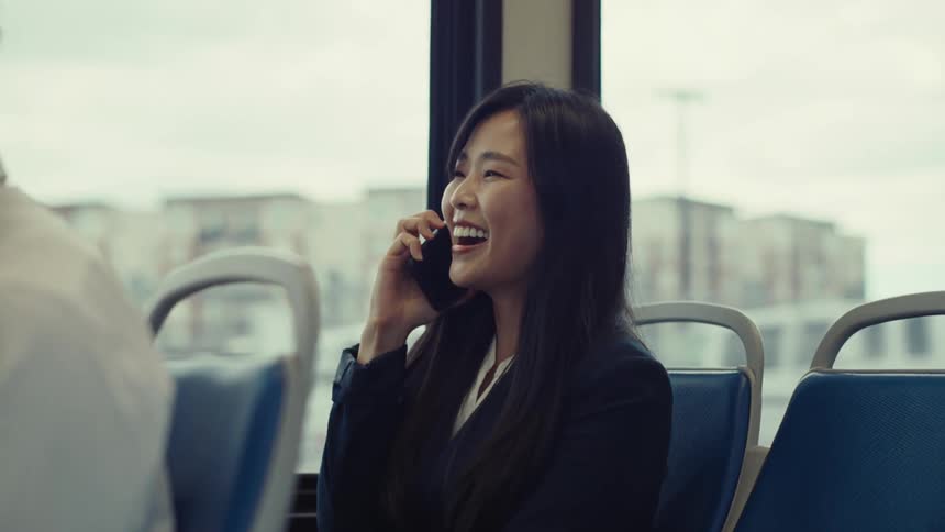 Woman riding on a bus smiles while talking on her smartphone