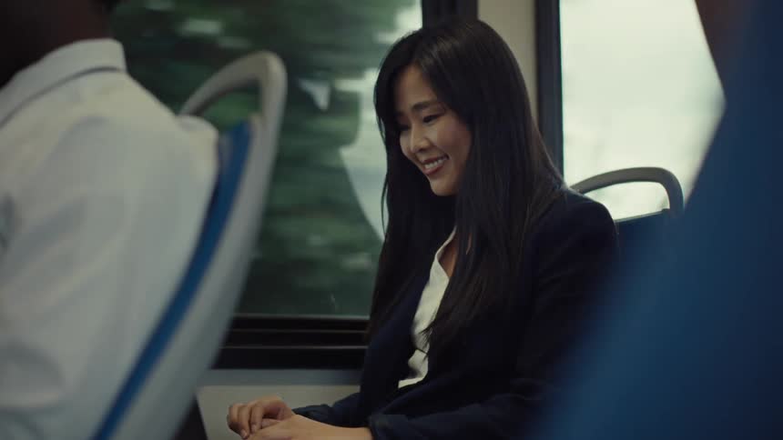 A woman on public transportation smiles as she opens her laptop and starts typing