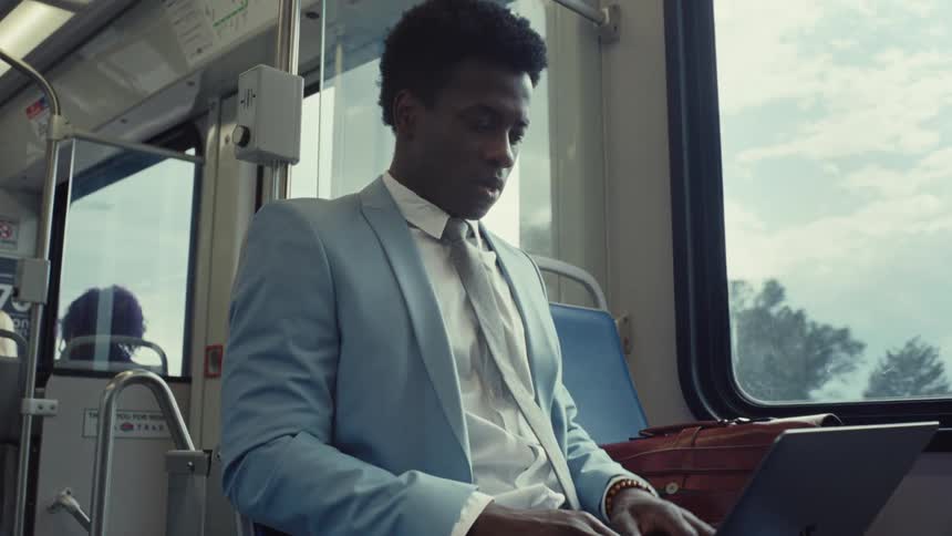 A man riding on a bus opens his laptop computer and begins typing