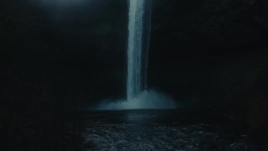 Water cascades over a cliff in a forest