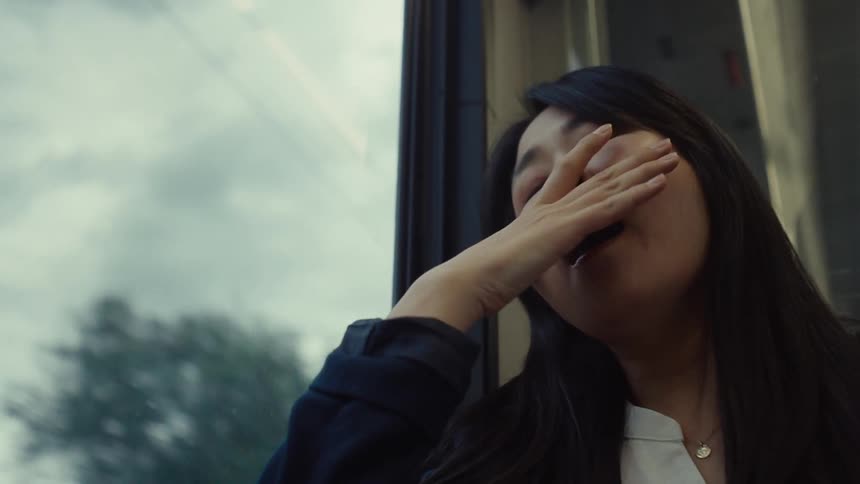 A woman yawns while looking out the train window