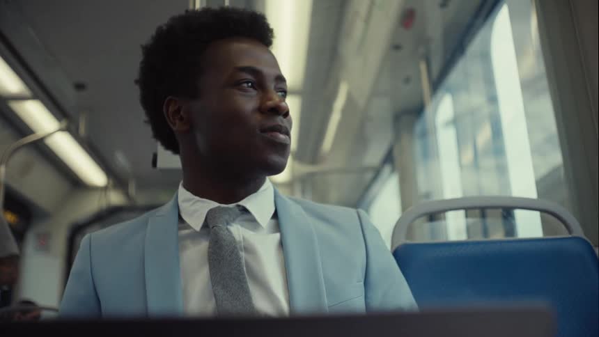A man has a small smile on his face as he looks out the window of a train