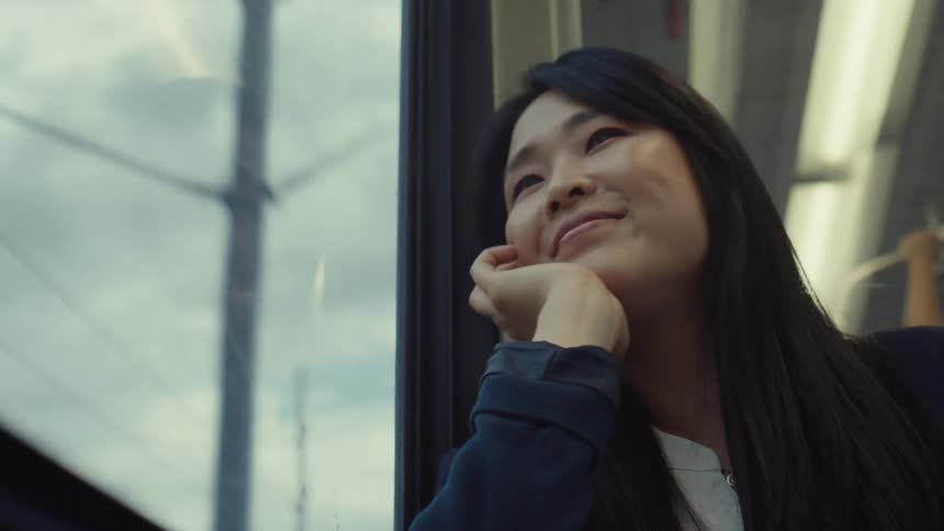 A woman smiles while looking out of the window on the moving train