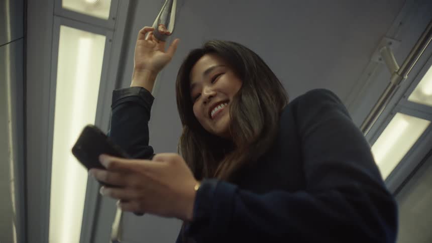Woman standing on public transportation smiles while scrolling on her smartphone