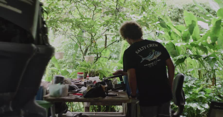 A man working with tools is standing at a table when another man walks up to him