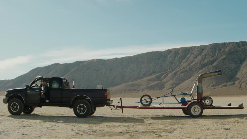 A man drives up in a pickup truck towing a buggy on a trailer