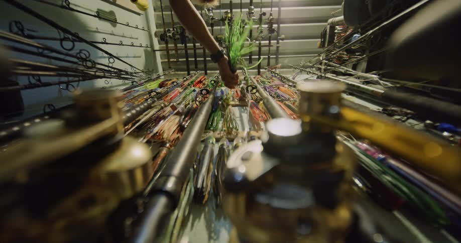 A person is reaching for a fishing lure among an extensive collection of fishing rods and lures organized in a storage area