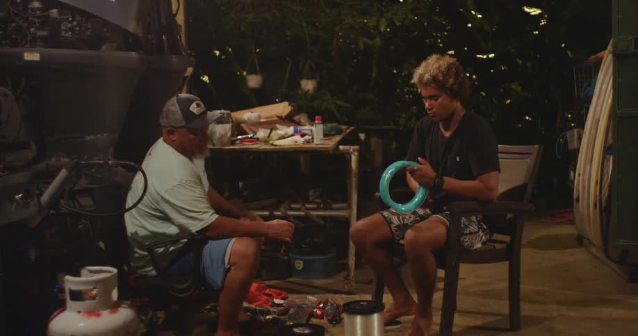 Two men sit quietly facing each other as one winds wire in a loop
