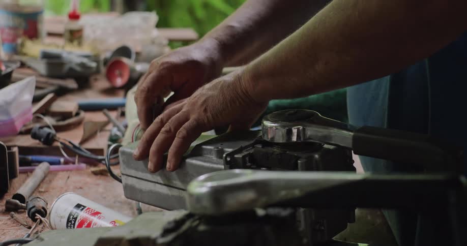 A man is working on a mechanical device possibly an engine or motor on a cluttered workbench with various tools and parts scattered around