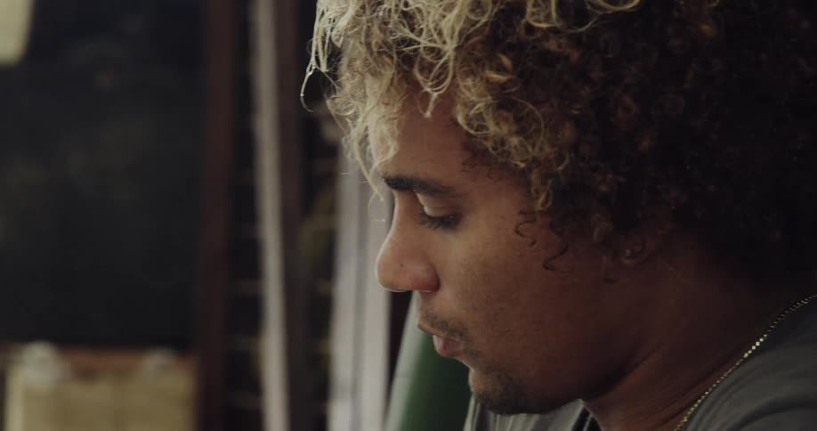 Man in profile with curly hair and blonde highlights in a bright indoor environment