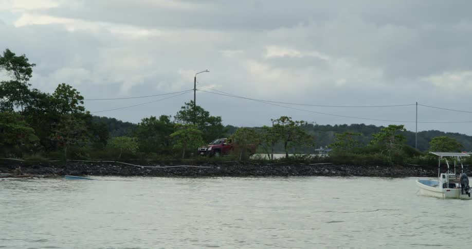 Person drives a red truck along a waterfront road paralleling power lines on a cloudy day