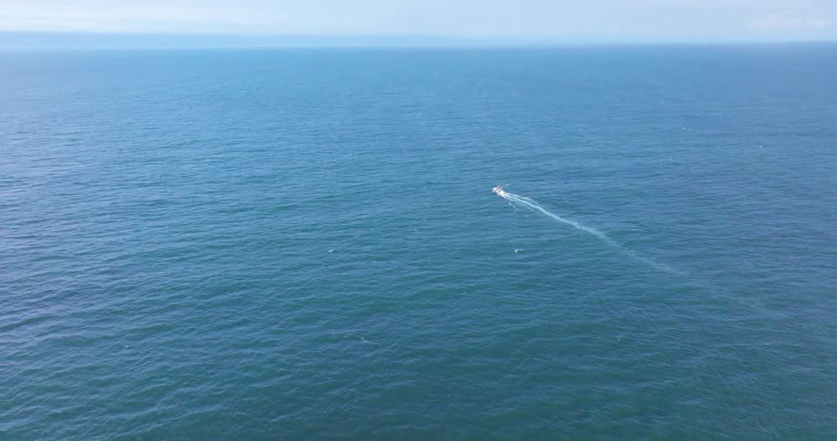 A small boat cuts through the vast expanse of the blue ocean leaving a foamy wake in its path
