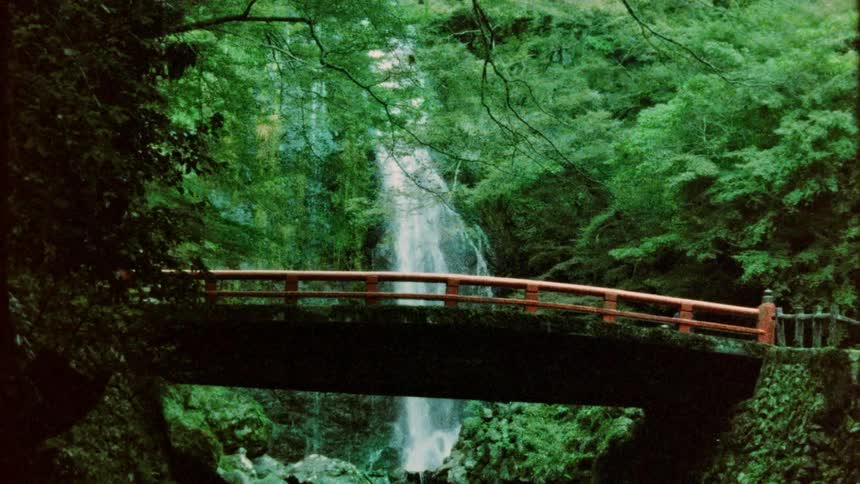 A man walks up to a bridge that crosses a river next to a waterfall