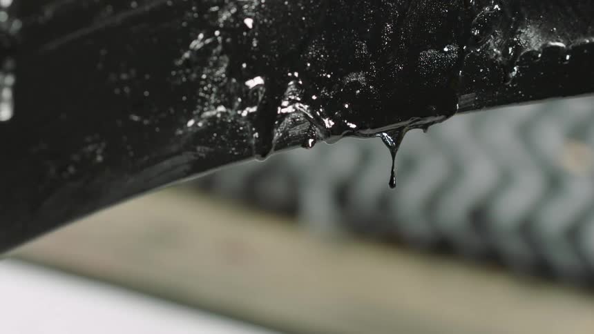 A closeup of a black tar like viscous liquid dripping from a surface